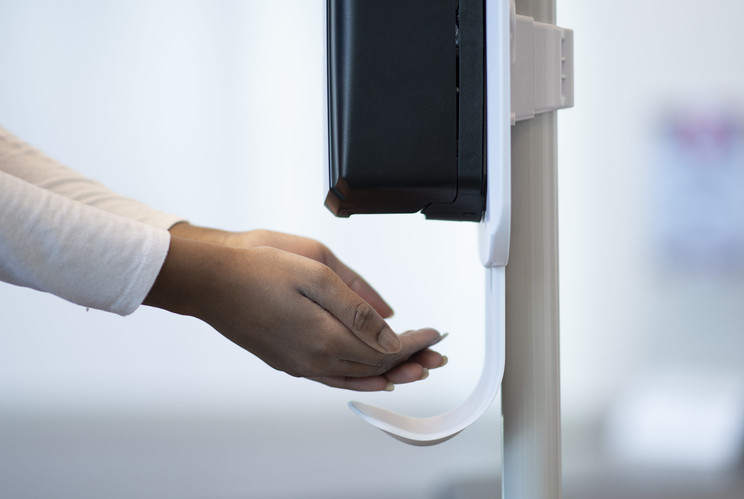 Female medical professional putting their hands under an automatic sanitizer dispenser at the hospital to ensure their hands are clean and germ free.